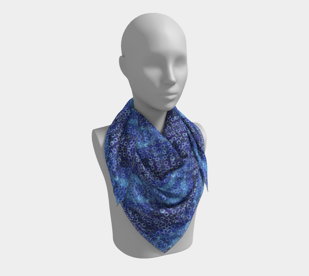 Mannequin wearing a square scarf of shades of blue and purple with light blue rings printed all over