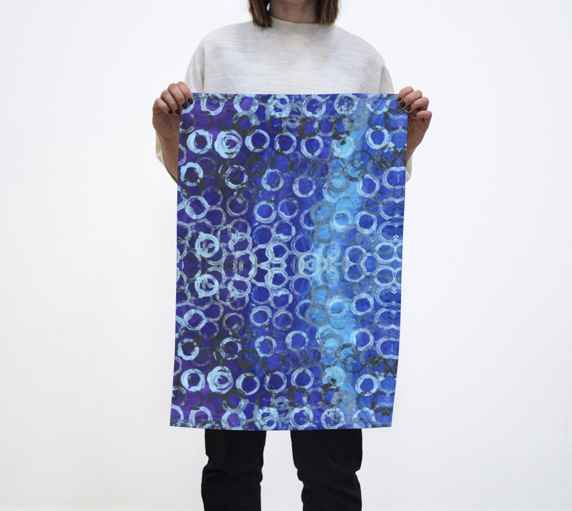 Tea towel with a background of varying shades of blue, with the darker hues dominating, are dozens of rings; most are white, but about a tenth of them are black