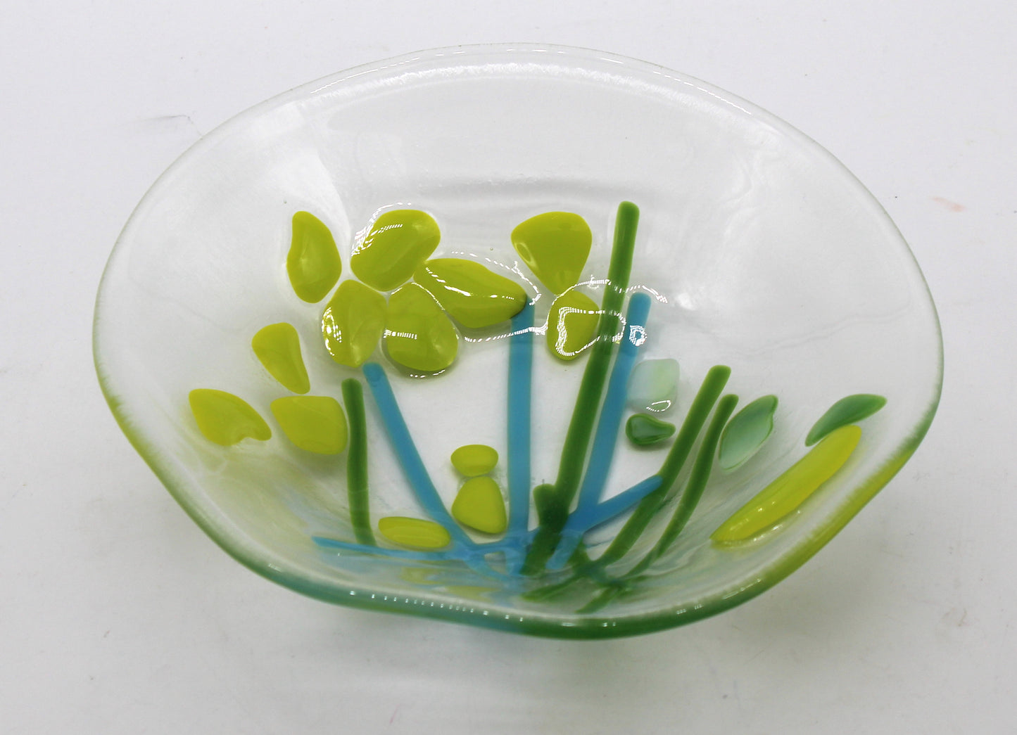 This is a fused glass piece that is clear with blue and green lines resembling stems, and lime green blotches resembling flowers.