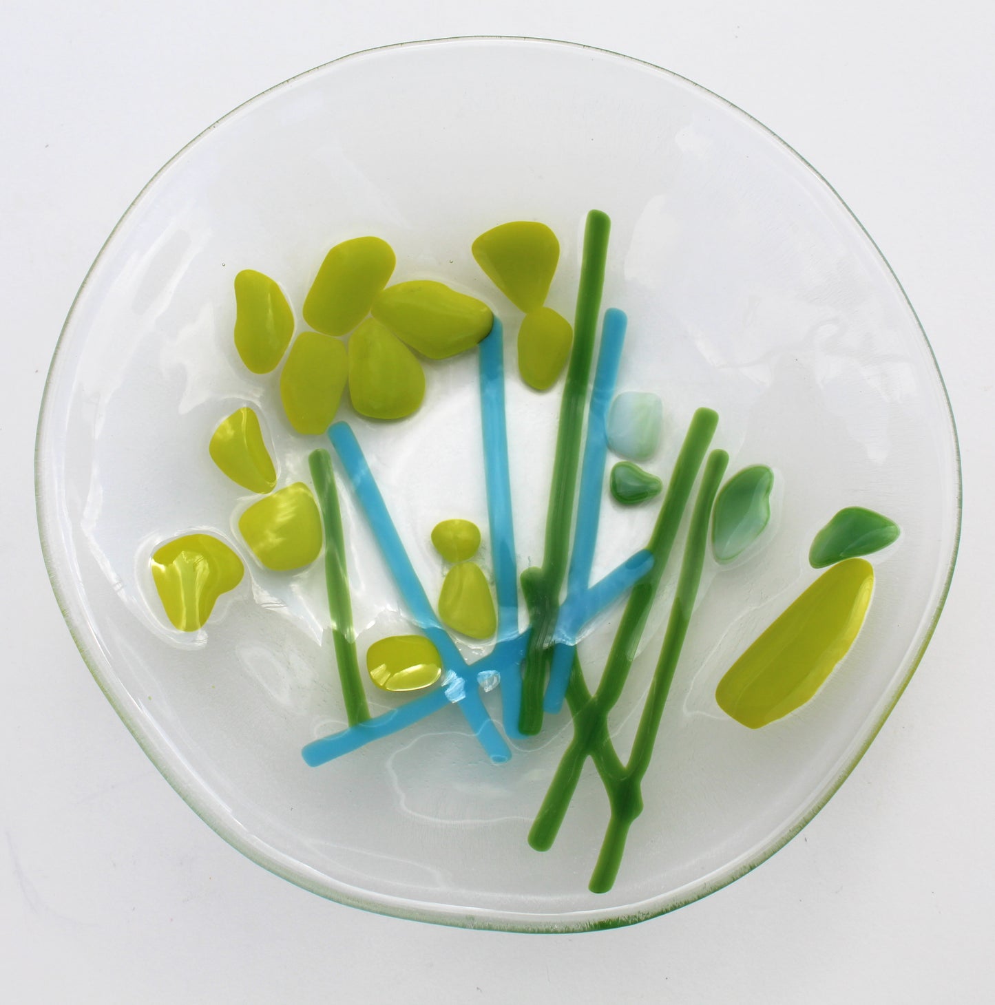 This is a fused glass piece that is clear with blue and green lines resembling stems, and lime green blotches resembling flowers.