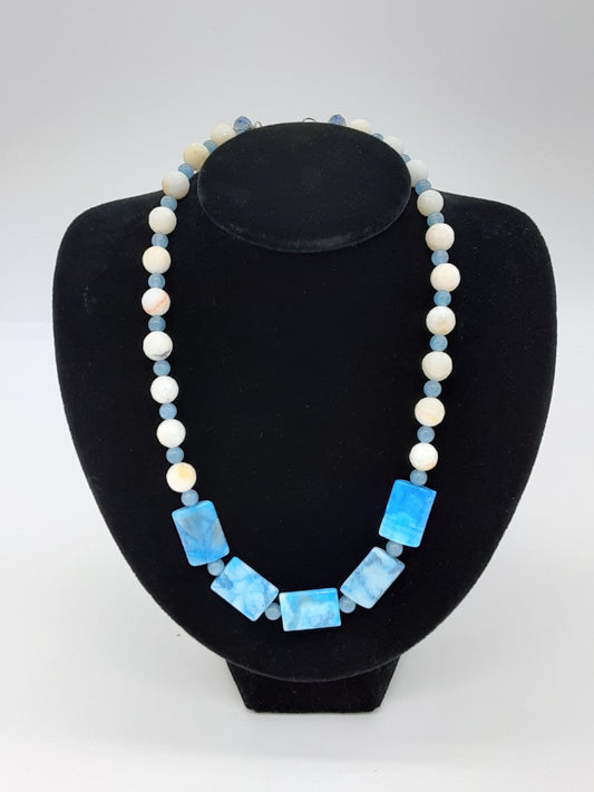 alternating light blue and white beads around most of the necklace. the center has 5 larger rectangle light blue marbled beads 