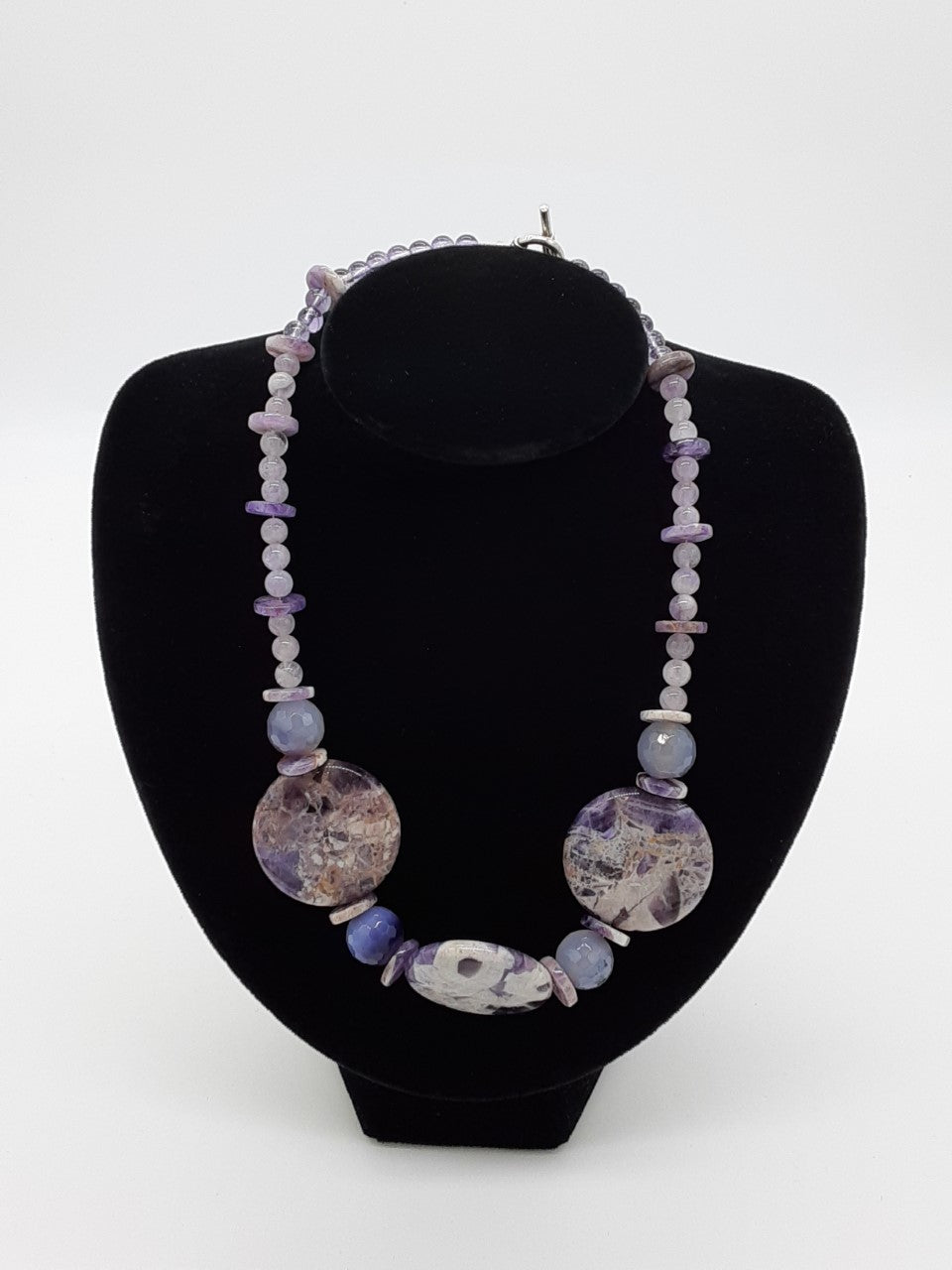 necklace made with purple quartz. Mostly round beads with a a few disks. The center has three large flat beads of purple and white pattern