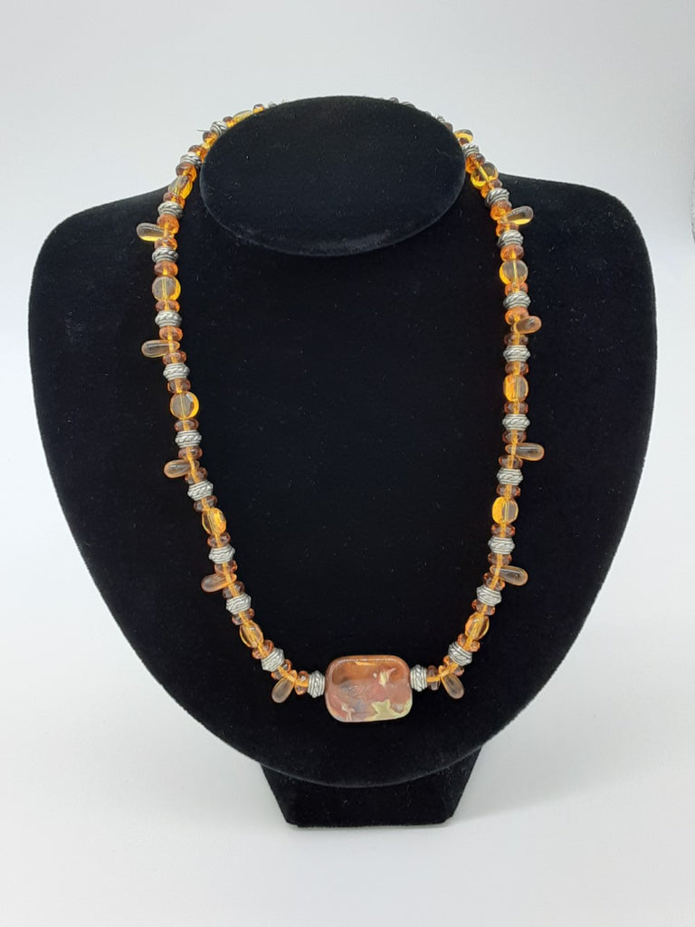 Necklace that is mostly light browns with some silver and a large semi precious gem stone in the center