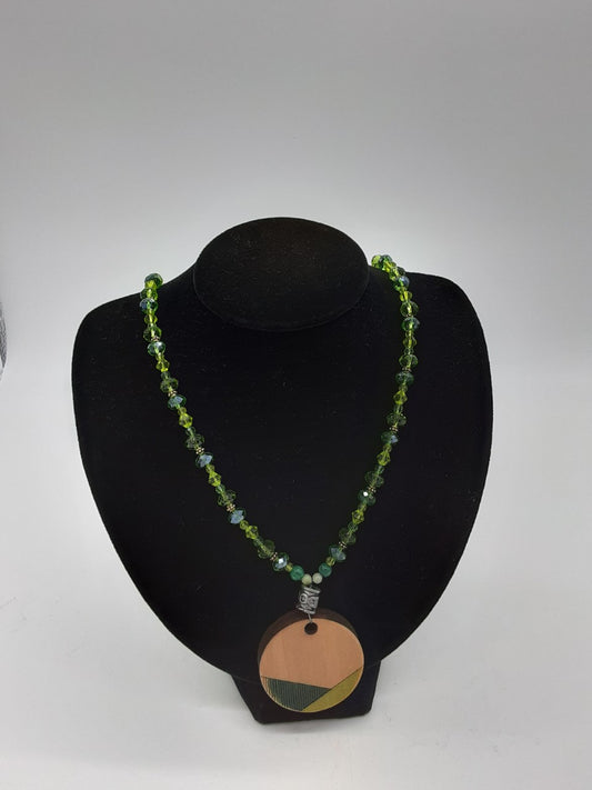 necklace made with faceted green beads with a wooden etched pendant that is accented green 