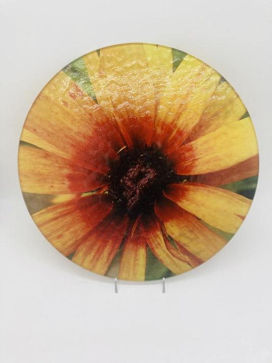 This is a round acryllic cutting board with a photo of a yellow flower with a red center