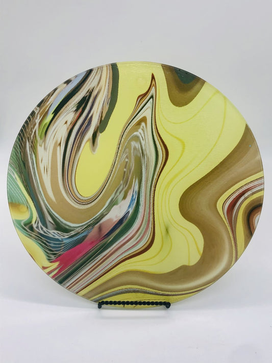 Circular glass cutting board with swirling design of yellow, gold, green, pink swirl