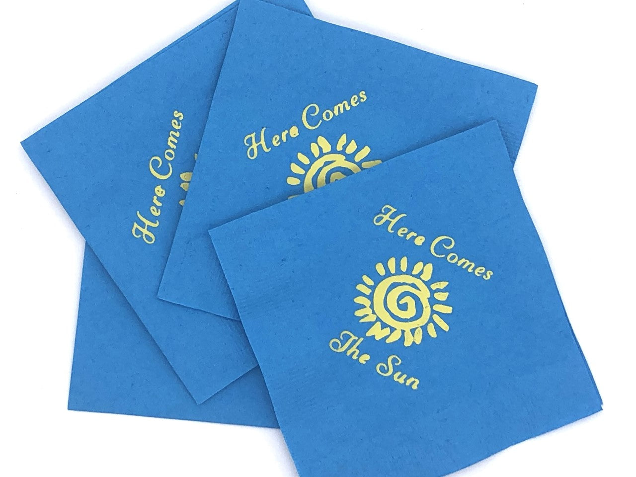 Light blue napkins with yellow sun and Here Comes the Sun slogan