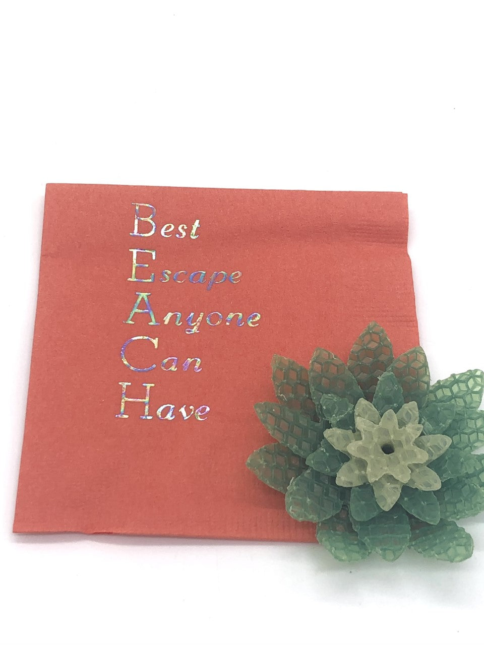 Coral cocktail napkins with iridescent Best Escape Anyone Can Have slogan. The first letter of each word spells the word BEACH vertically