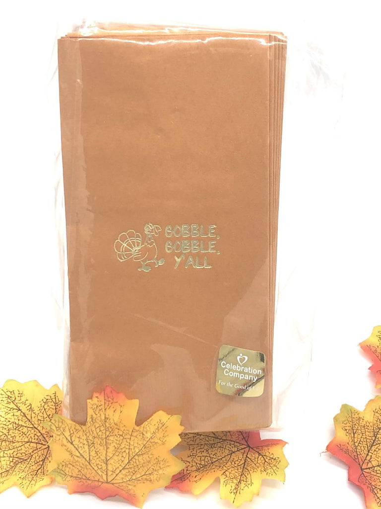 Light brown dinner napkins with a gold turkey to the left of Gobble, Gobble, Y'all slogan in gold