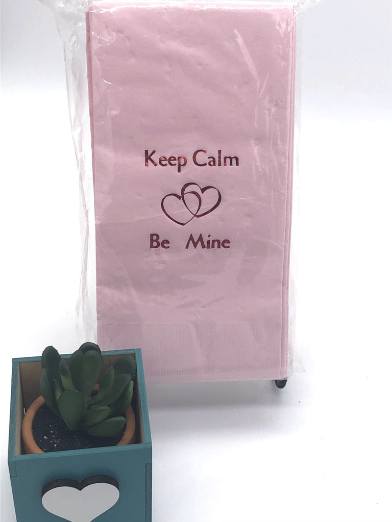 Light pink dinner napkins with dark pink Keep Calm Be Mine slogan above and below two interlocked hearts