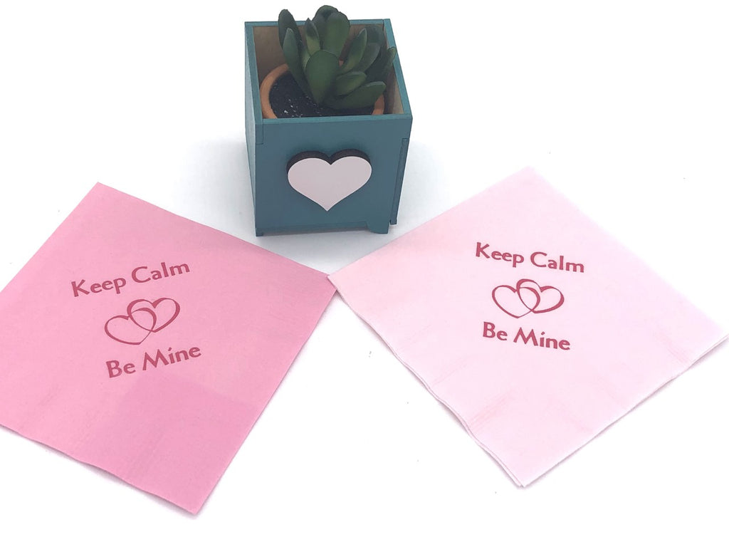 Two shades of pink cocktail napkins with dark pink Keep Calm Be Mine slogan above and below two interlocked hearts