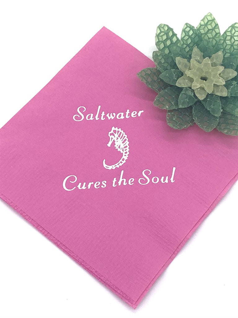 Pink cocktail napkin with white seahorse and Saltwater Cures the Soul slogan