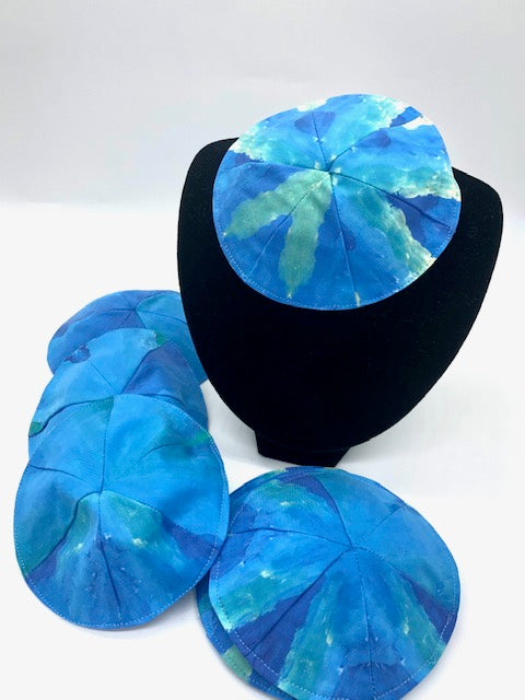 several blue and green striped kippot, one on a velvet stand